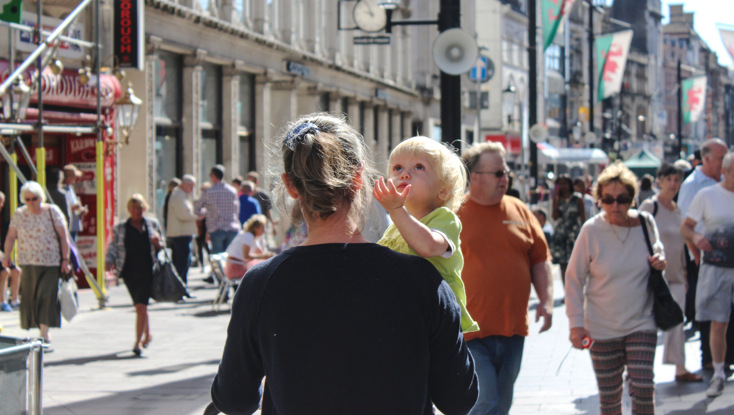 Young child in adults arms being carried looking up the sky in city