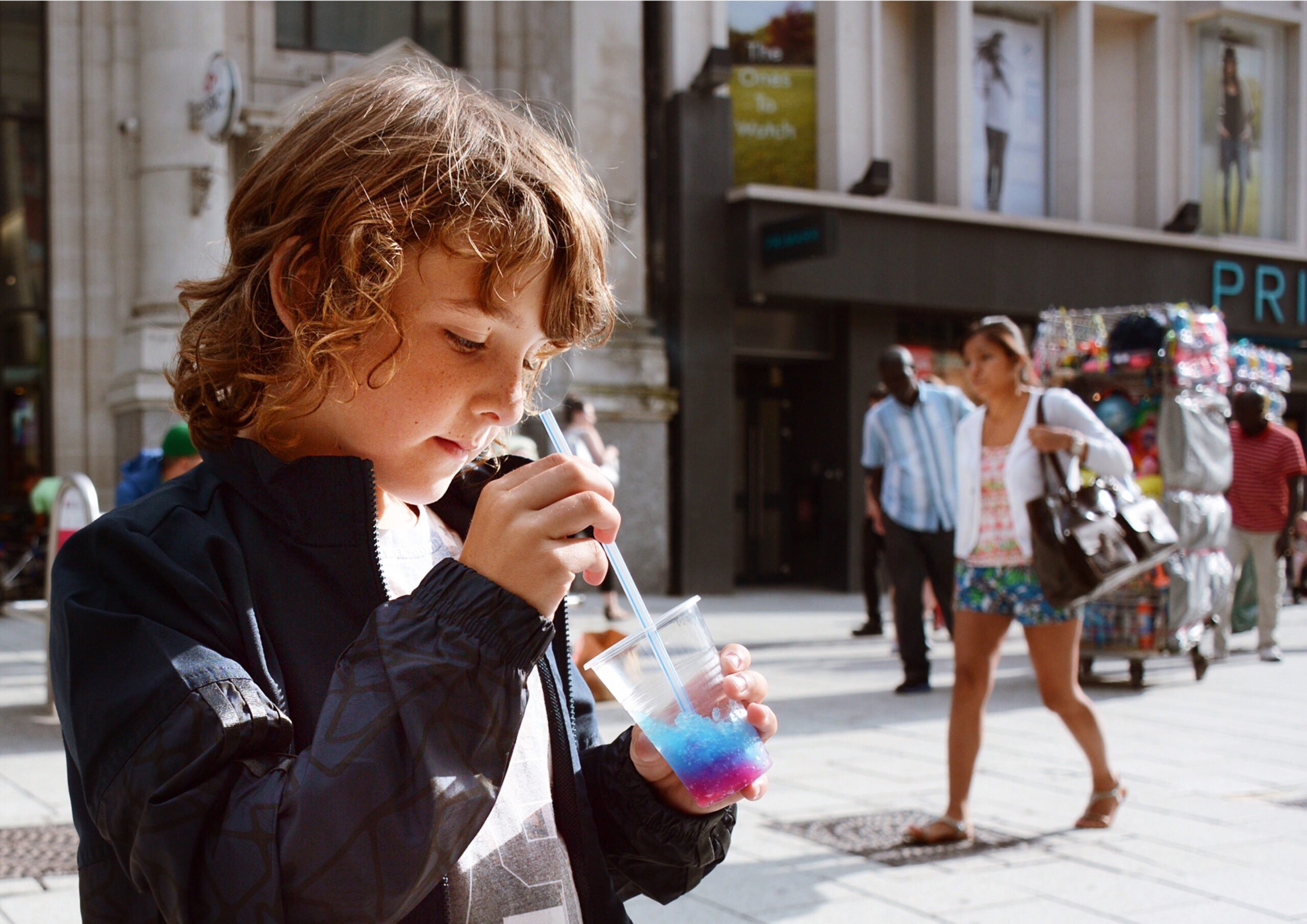 Long haired young boy in city centre with slush drink